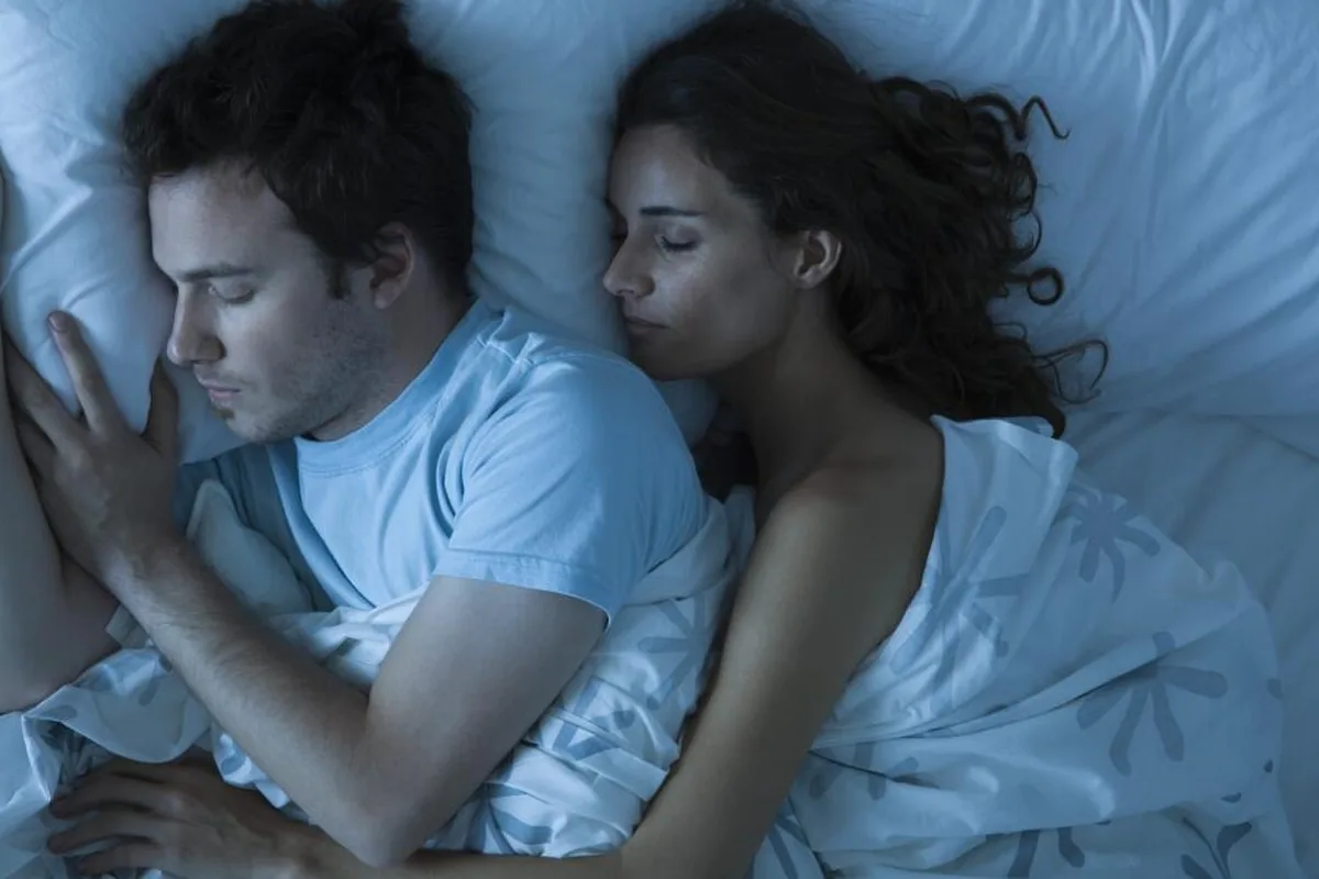 A couple asleep side by side in bed in cool blue night light