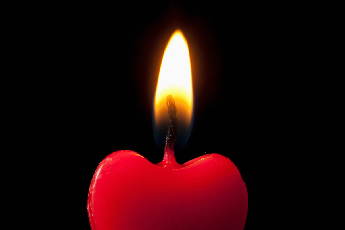 A single heart-shaped red candle burning against a black background
