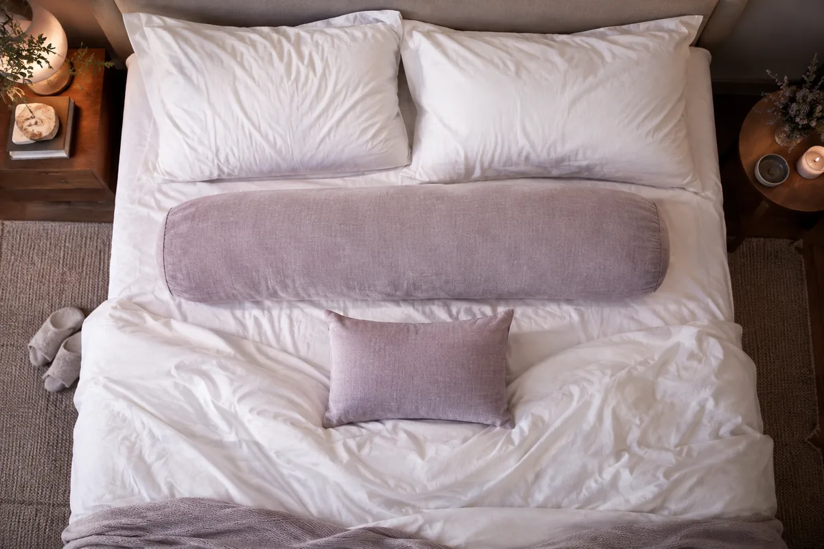 A long body pillow and a small pillow arranged on a bed